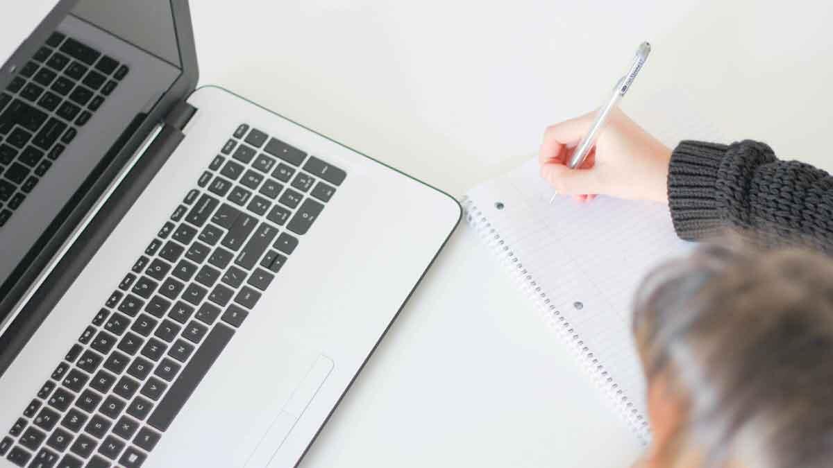 student laptop writing notes on paper