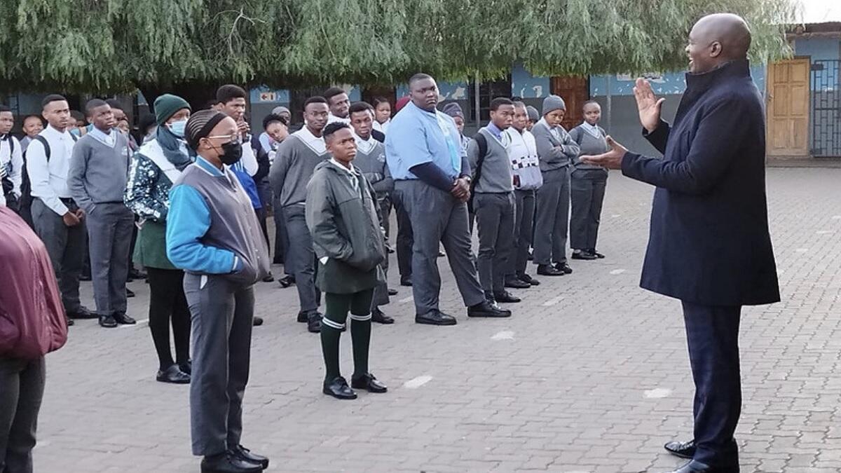 New school teacher stands in assembly with learners