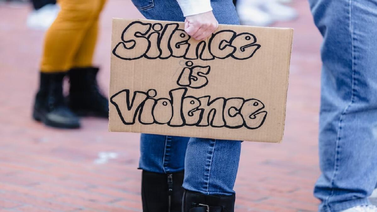 A women holding a "silence is violence" sign at a protest against gender-based violence