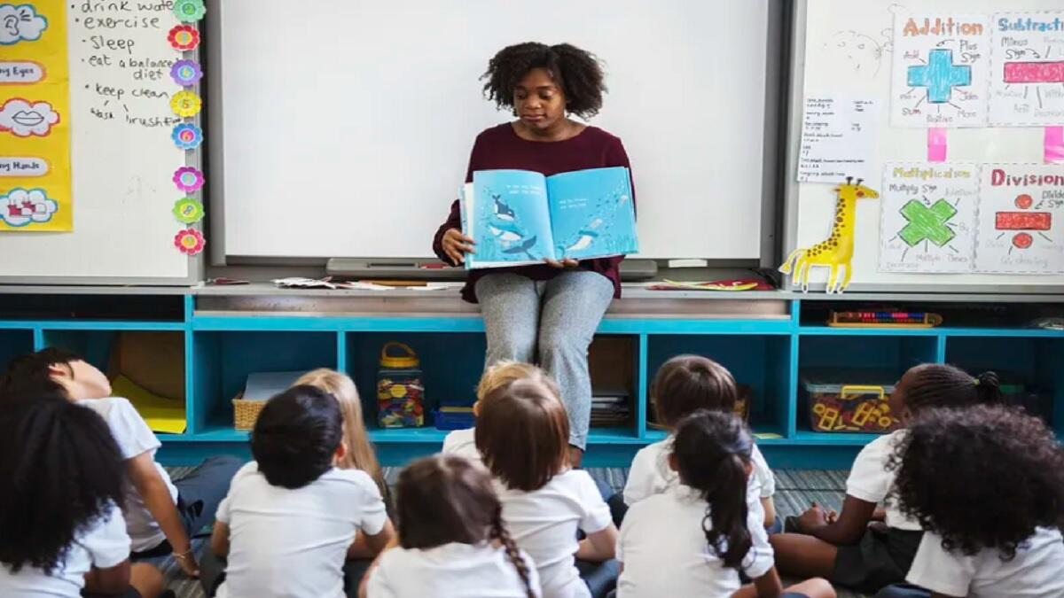 Teacher's assistant reading a book to primary school learners 
