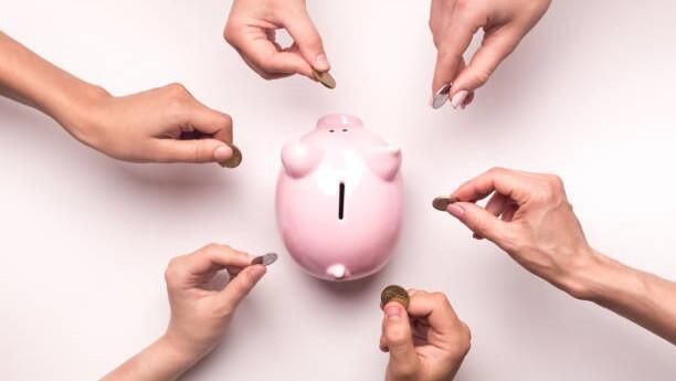 Multiple different hands putting coins into a piggy bank